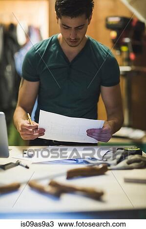 Stock Image - Young man holding paper work, looking down. Fotosearch