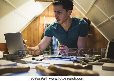 Picture - Young man leaning against workbench using digital tablet. Fotosearch