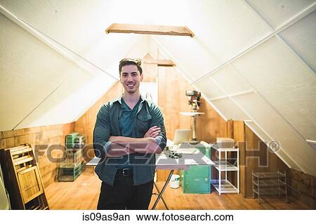 Young man standing in workspace, arms folded, looking at camera smiling View Large Photo Image Picture - Young man standing in workspace, arms folded, looking at camera smiling. Fotosearch