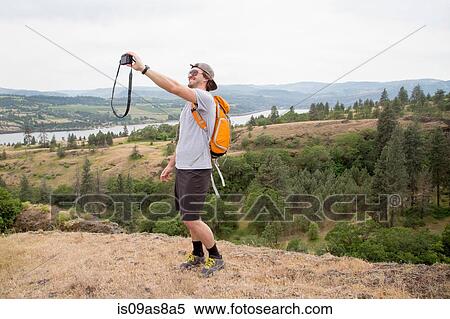 Young man, standing on top of mountain, taking self portrait with camera View Large Photo Image Stock Photography - Young man, standing on top of mountain, taking self portrait with camera. Fotosearch