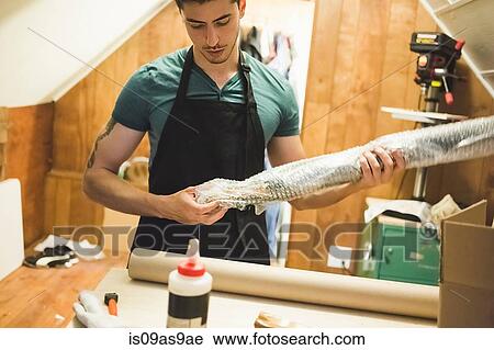 Stock Image - Young man using bubble wrap to prepare parcel for delivery. Fotosearch