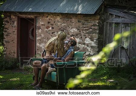 Stock Image - Young woman in bikini sitting on boyfriends lap shaving his chin at holiday cottage. Fotosearch