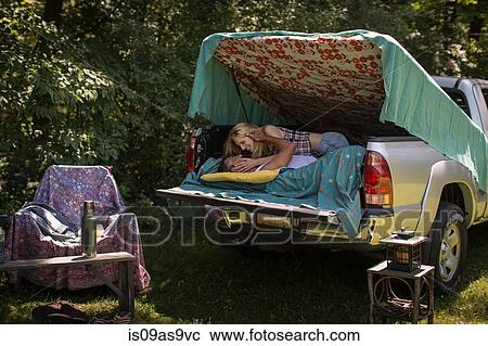 Stock Image - Young woman kissing boyfriend in pick up boot whilst camping. Fotosearch
