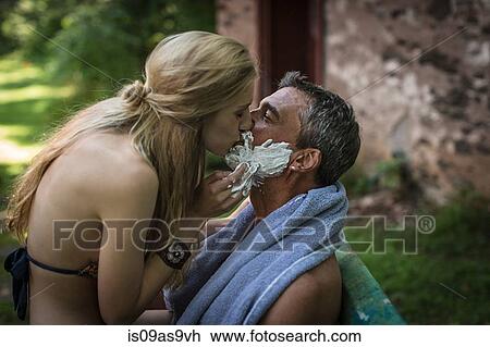 Stock Image - Young woman kissing boyfriend with shaving cream on chin at holiday cottage. Fotosearch