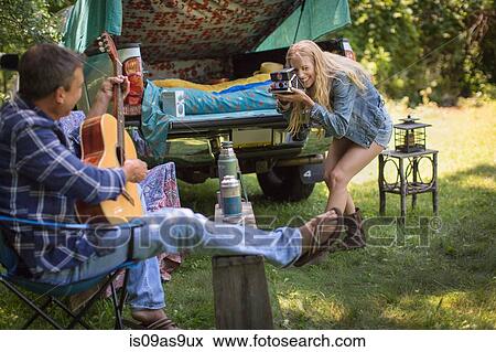 Young woman photographing boyfriend playing acoustic guitar whilst camping View Large Photo Image Stock Photo - Young woman photographing boyfriend playing acoustic guitar whilst camping. Fotosearch