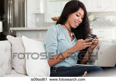 Young woman, relaxing on sofa, laptop on lap, holding smartphone View Large Photo Image Stock Image - Young woman, relaxing on sofa, laptop on lap, holding smartphone. Fotosearch