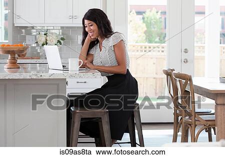 Young woman, sitting at kitchen counter with coffee and laptop View Large Photo Image Stock Image - Young woman, sitting at kitchen counter with coffee and laptop. Fotosearch