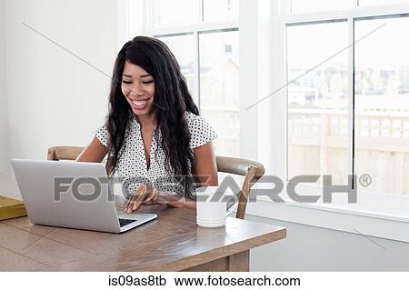 Stock Image - Young woman, sitting at table with coffee and laptop. Fotosearch