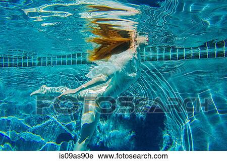Stock Image - Young woman swimming underwater, wearing thin white shirt. Fotosearch