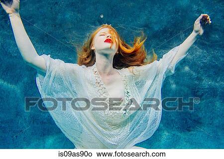 Picture - Young woman underwater, wearing thin white shirt. Fotosearch