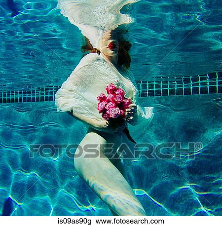 Stock Image - Young woman underwater, wearing thin white shirt and holding flowers. Fotosearch