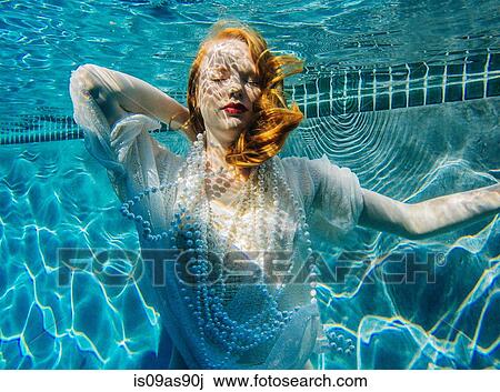 Stock Image - Young woman underwater, wearing thin white shirt and pearls. Fotosearch