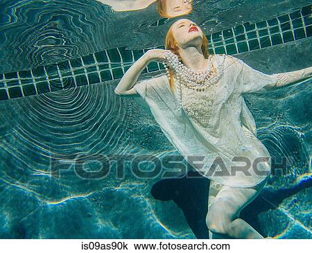 Stock Image - Young woman underwater, wearing thin white shirt and pearls. Fotosearch
