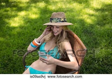 Young woman wearing bikini and sunhat reading smartphone texts in garden View Large Photo Image Stock Image - Young woman wearing bikini and sunhat reading smartphone texts in garden. Fotosearch