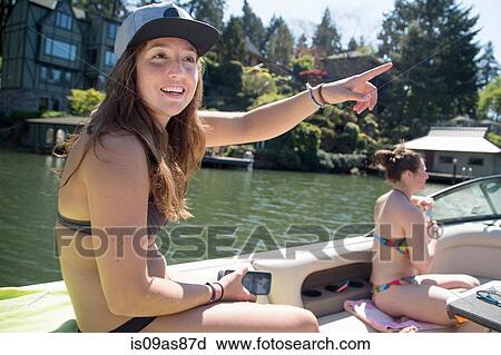 Stock Image - Young woman wearing bikini pointing from motor boat, Lake Oswego, Oregon, USA. Fotosearch