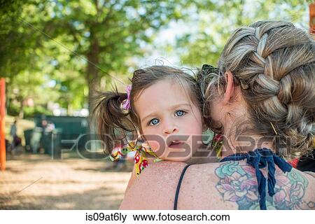Stock Photo - Baby girl looking over mothers shoulder at camera. Fotosearch