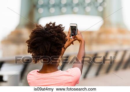 Stock Photo - Back view of young woman taking selfie. Fotosearch
