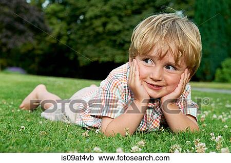 Stock Image - "Boy lying on grass, chin in hands lying on grass looking away smiling". Fotosearch