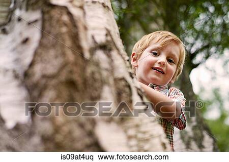 Stock Photography - "Boy peeking from behind tree, looking at camera smiling". Fotosearch