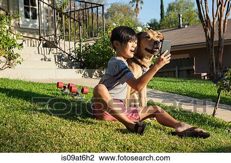 Stock Image - Boy posing for smartphone selfie with dog in garden. Fotosearch