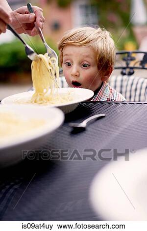 "Boy sitting at garden table being served spaghetti, looking surprised" View Large Photo Image Stock Photo - "Boy sitting at garden table being served spaghetti, looking surprised". Fotosearch