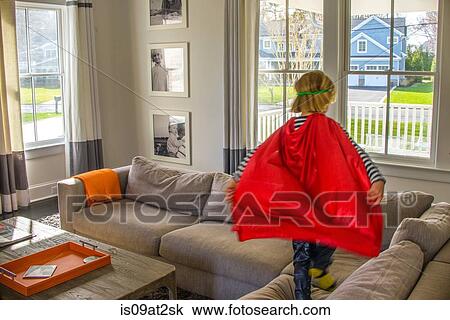 Stock Image - Boy with red cape playing on sofa. Fotosearch
