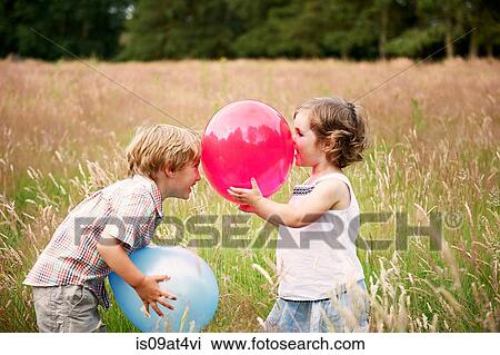 Stock Image - Brother and sister in tall grass face to face playing with balloon. Fotosearch