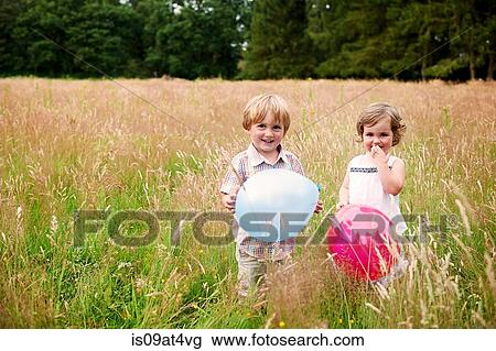 Brother and sister in tall grass holding balloon looking at camera smiling View Large Photo Image Stock Image - Brother and sister in tall grass holding balloon looking at camera smiling. Fotosearch