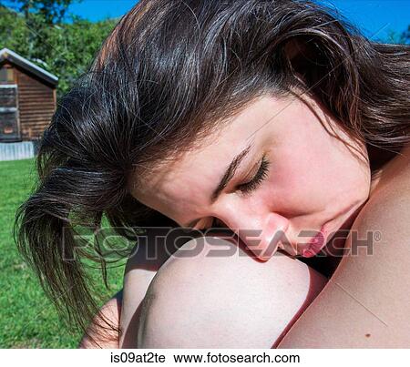 Stock Image - Close up of woman hugging knees with eyes closed. Fotosearch