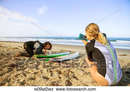 "Couple on beach, young woman taking photograph of man with surfboard" View Large Photo Image Stock Photo - "Couple on beach, young woman taking photograph of man with surfboard". Fotosearch