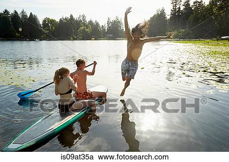Stock Image - "Couple paddling boat, man jumping into lake, Seattle, Washington, USA". Fotosearch