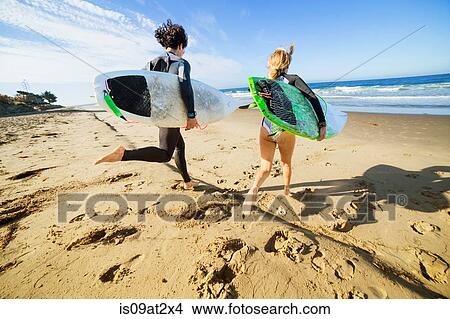 Picture - "Couple running towards sea, carrying surfboards, rear view". Fotosearch
