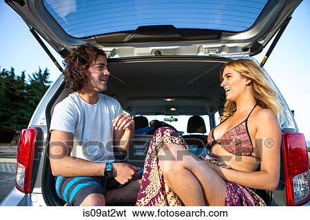 Stock Photograph - "Couple sitting in boot of car, face to face, smiling". Fotosearch