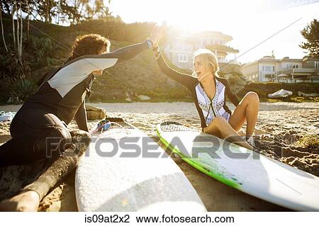 "Couple sitting on beach, clapping hands in high five, surfboards beside them" View Large Photo Image Stock Image - "Couple sitting on beach, clapping hands in high five, surfboards beside them". Fotosearch