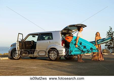 Stock Photograph - Couple taking surfboards from boot of car. Fotosearch