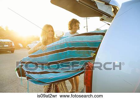 Stock Photography - Couple taking surfboards from boot of car. Fotosearch