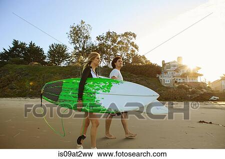 Stock Photo - "Couple walking towards sea, carrying surfboards". Fotosearch