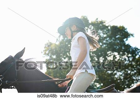 Stock Image - Cropped view of girl riding horse in countryside. Fotosearch