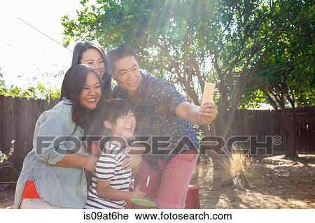 Stock Image - Family with boy posing for smartphone selfie in sunlit garden. Fotosearch