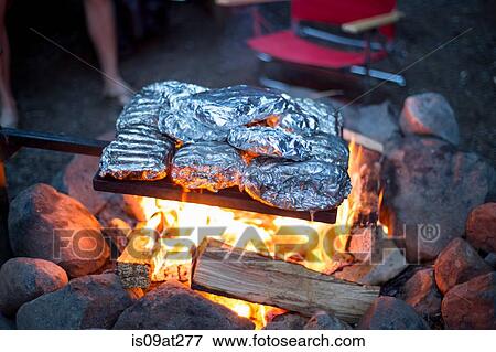 Stock Photo - Food wrapped in tin foil cooking over campfire. Fotosearch
