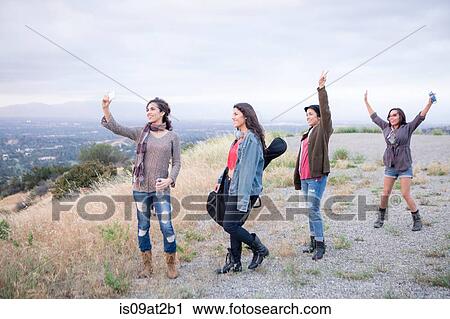 Stock Image - Four adult sisters posing for smartphone selfie on rural hill. Fotosearch