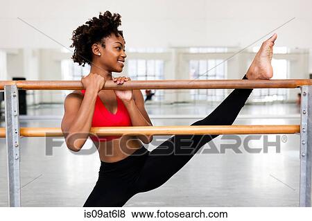 Front view of young woman holding barre leg raised looking away smiling View Large Photo Image Stock Photo - Front view of young woman holding barre leg raised looking away smiling. Fotosearch