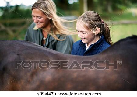 Girl and mother tending horse View Large Photo Image Stock Photograph - Girl and mother tending horse. Fotosearch