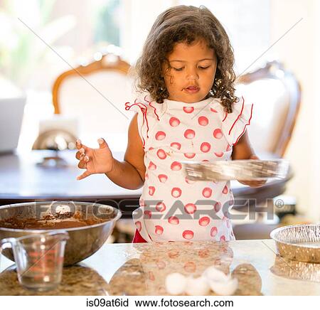 Stock Image - Girl at kitchen counter holding cake tin looking down. Fotosearch