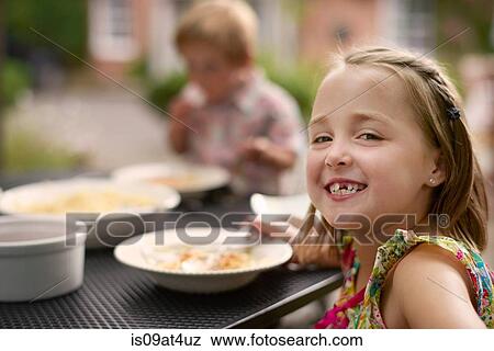 "Girl dining at garden table, looking over shoulder smiling at camera" View Large Photo Image Stock Photo - "Girl dining at garden table, looking over shoulder smiling at camera". Fotosearch