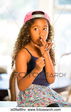 Stock Photo - Girl holding whisk licking cake mix off fingers looking away. Fotosearch