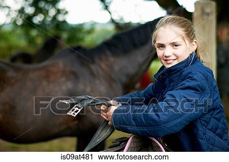 Stock Image - Girl horseback rider preparing saddle. Fotosearch