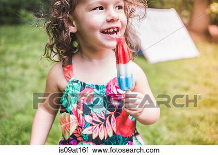 Stock Image - Girl in garden eating ice lolly. Fotosearch