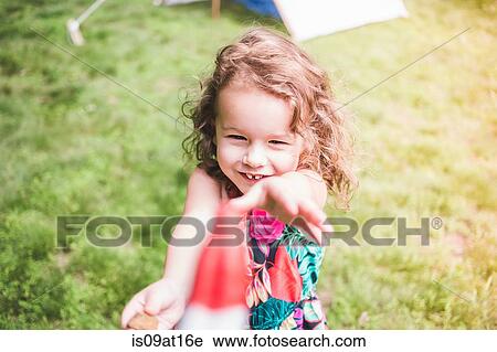Stock Image - Girl in garden reaching for ice lolly. Fotosearch