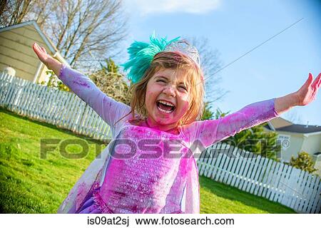Stock Image - Girl in gown with feather fascinator playing outdoors. Fotosearch